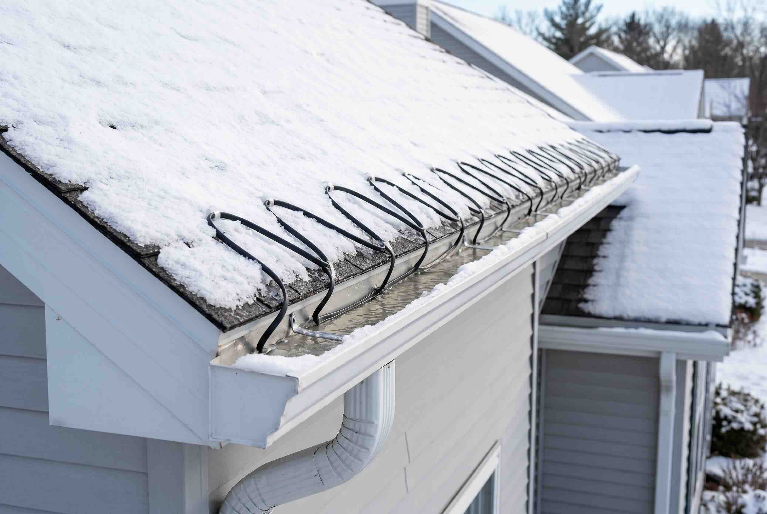 Heated cables installed in a zigzag pattern along a snow-covered roof eave and gutter.