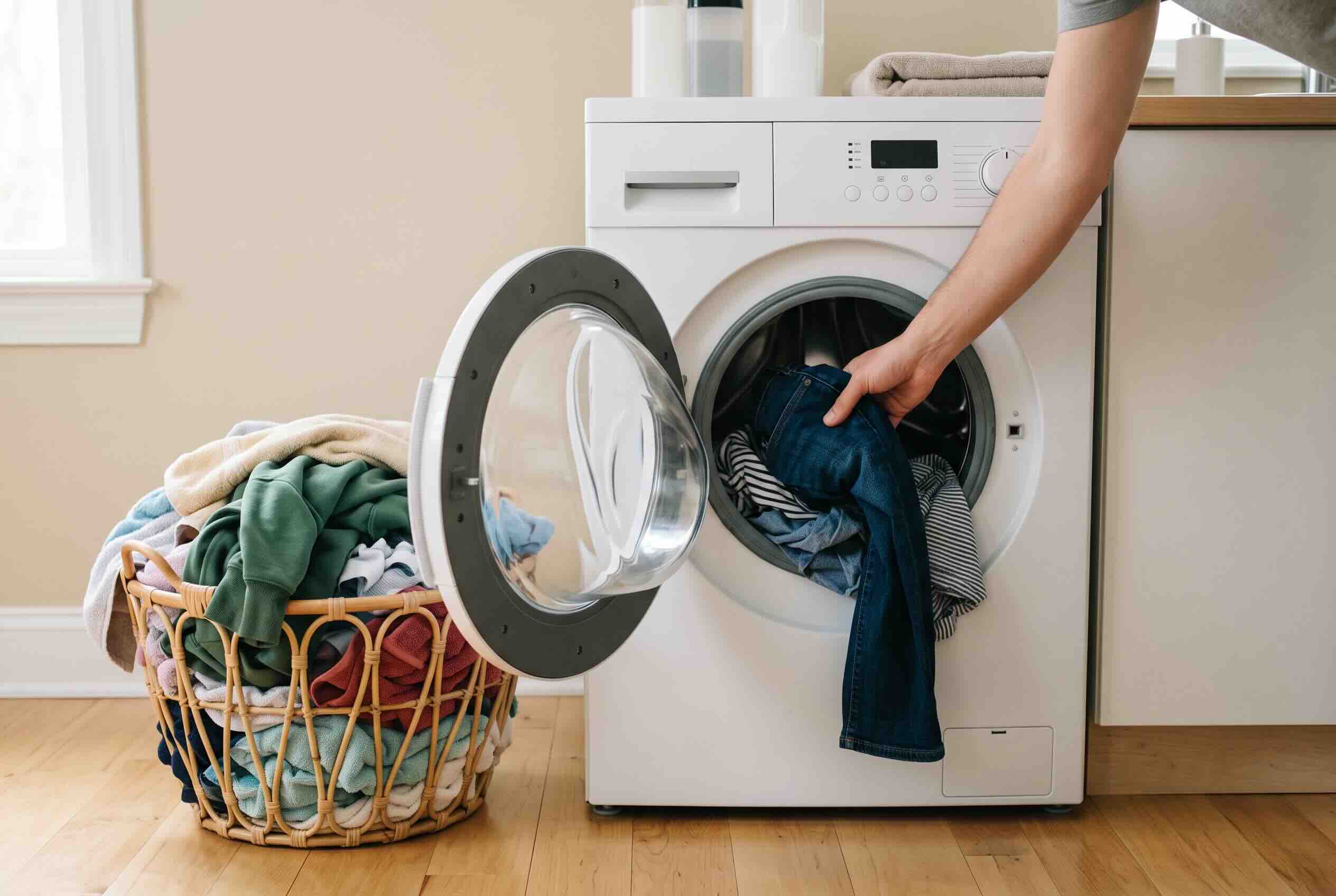 Loading clothes into a front-load washing machine next to a laundry basket.