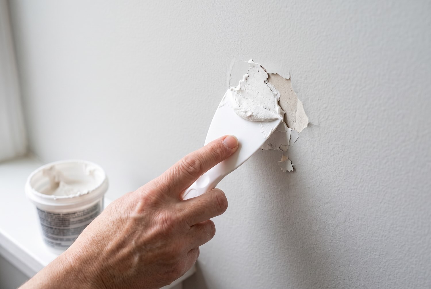 Patching a damaged section of drywall with spackle and a putty knife.