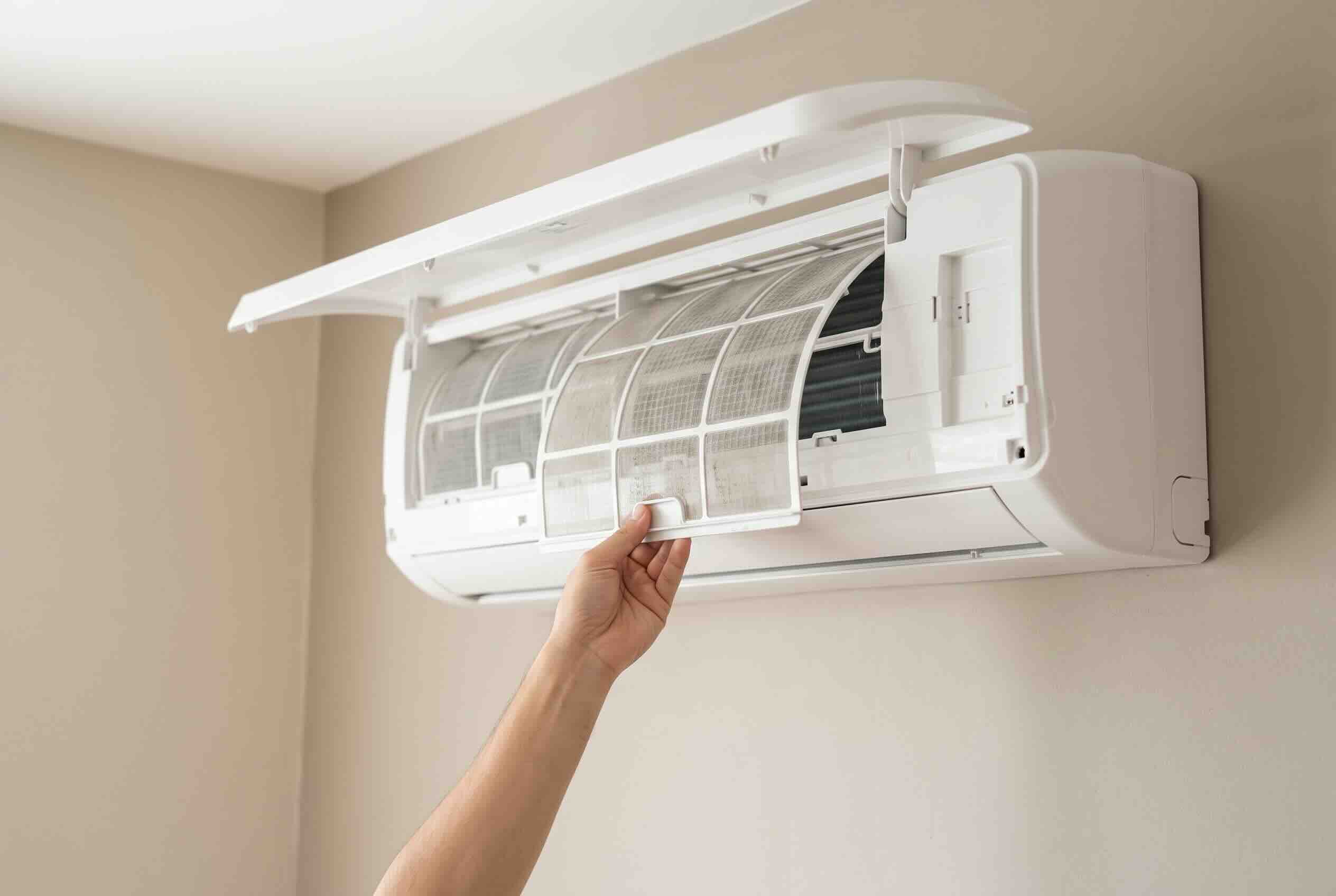Removing the front filter panel from a wall-mounted mini-split AC unit.