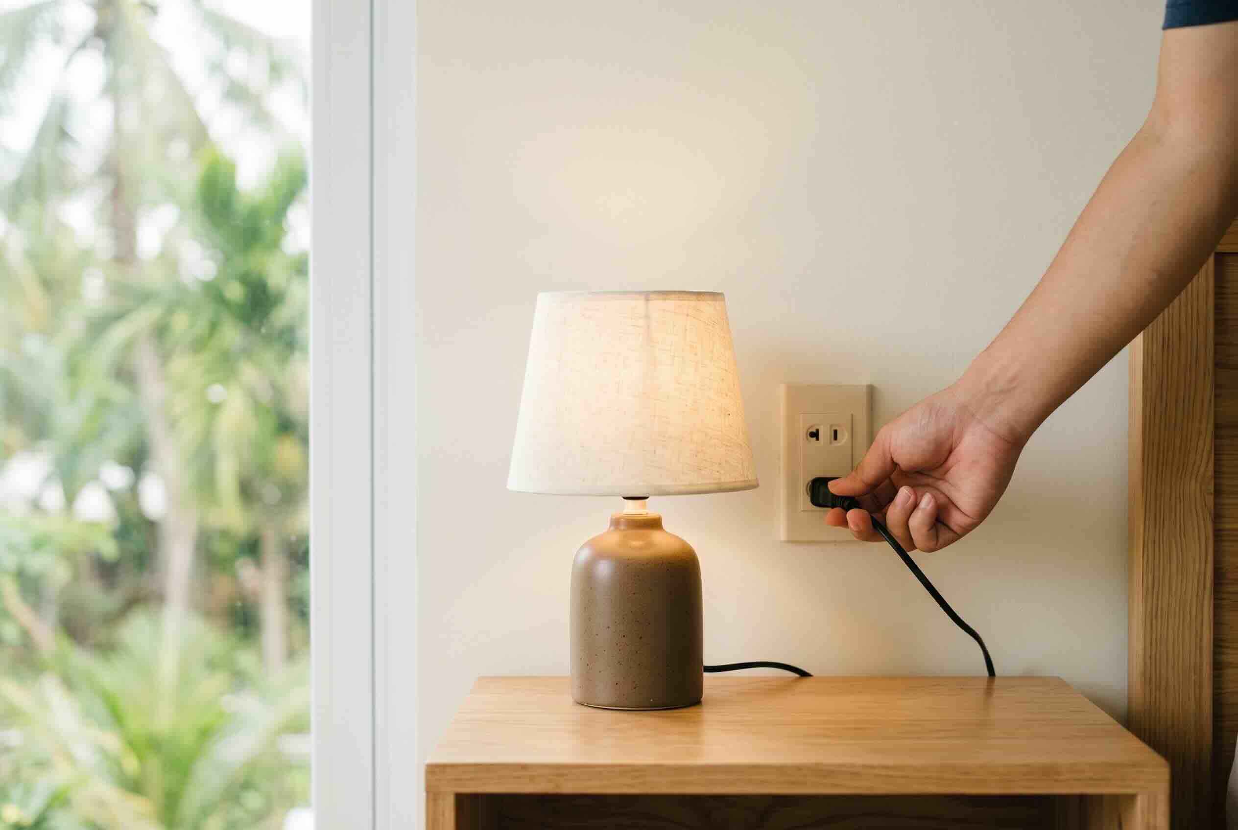 Testing a wall outlet by plugging in a small bedside lamp.