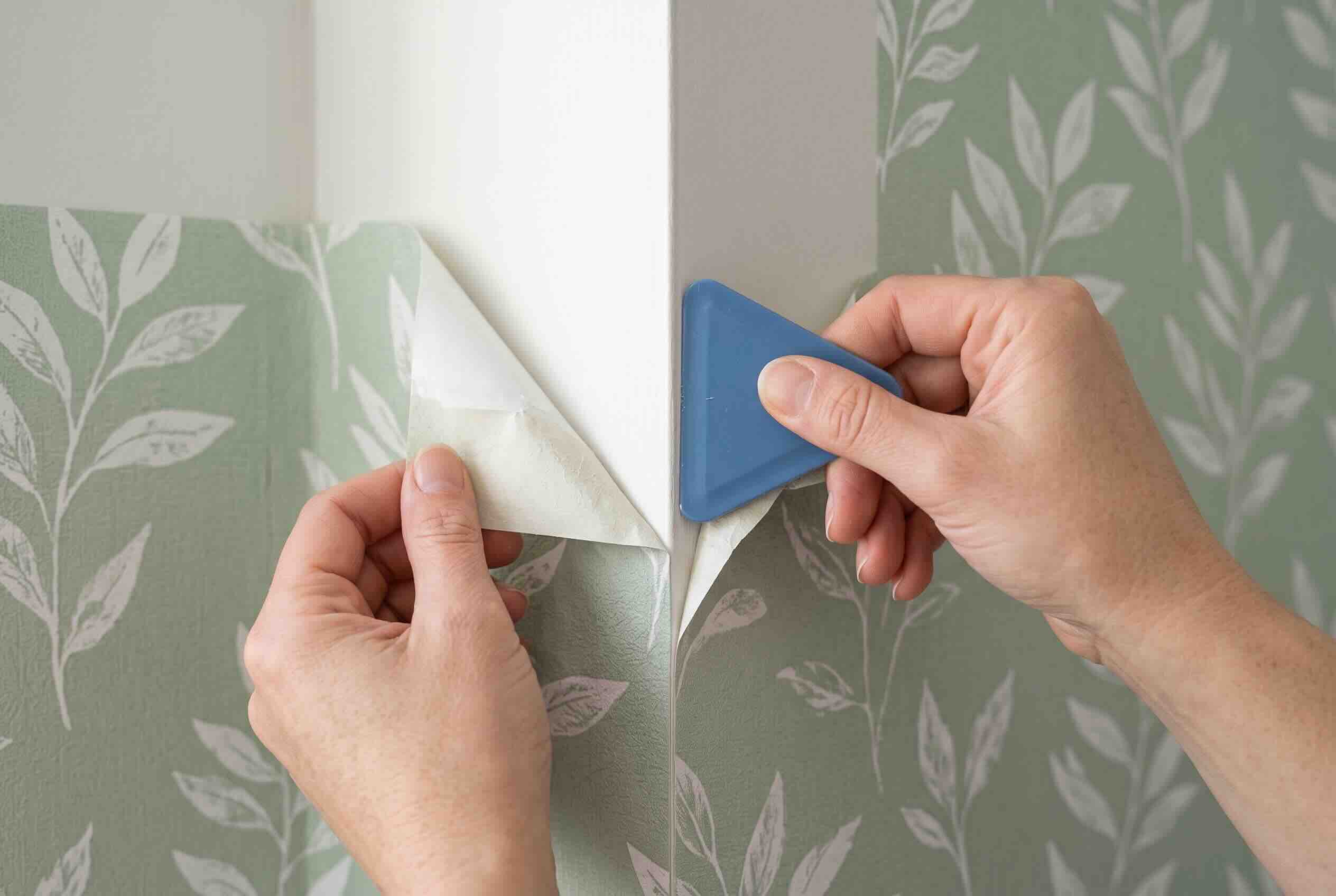 Using a plastic scraper to lift the top corner of the wallpaper to create a grippable flap.