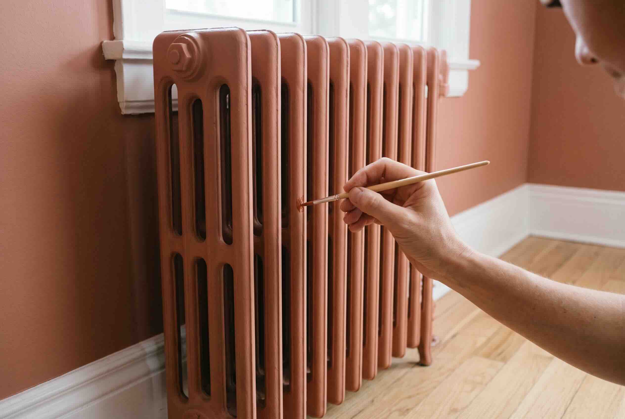 Using a small paintbrush to touch up a cast iron radiator painted a terracotta color.