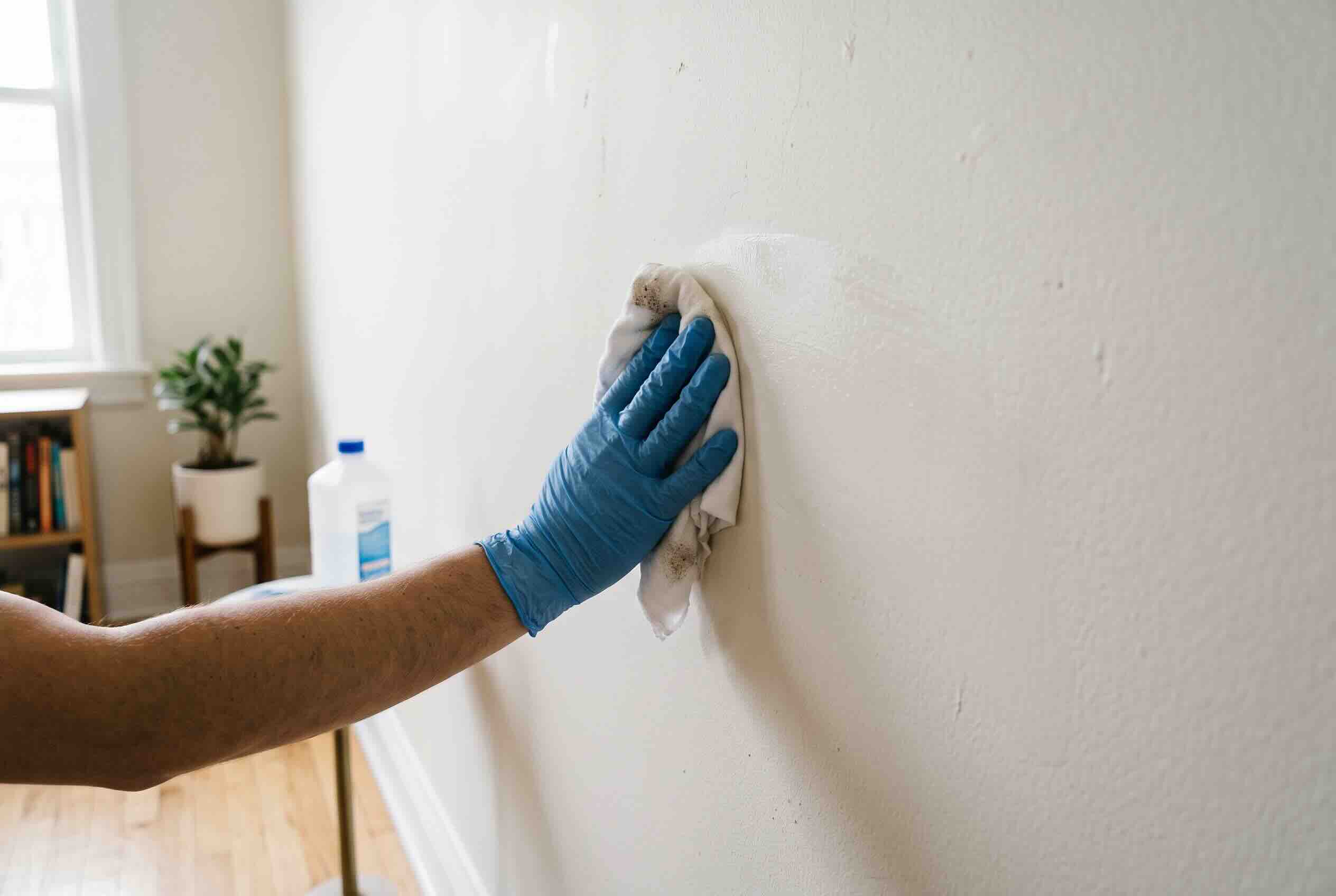 Wiping a wall clean with rubbing alcohol and a microfiber cloth.