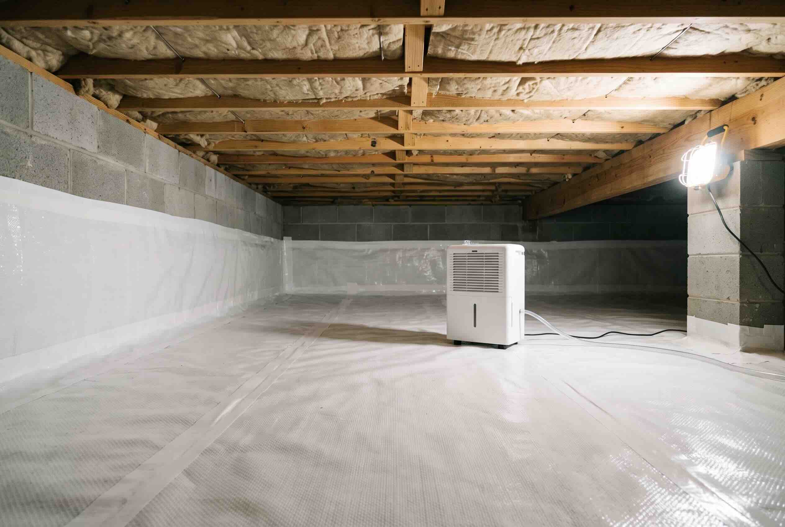A dehumidifier running on a white plastic vapor barrier in a clean, encapsulated crawl space.
