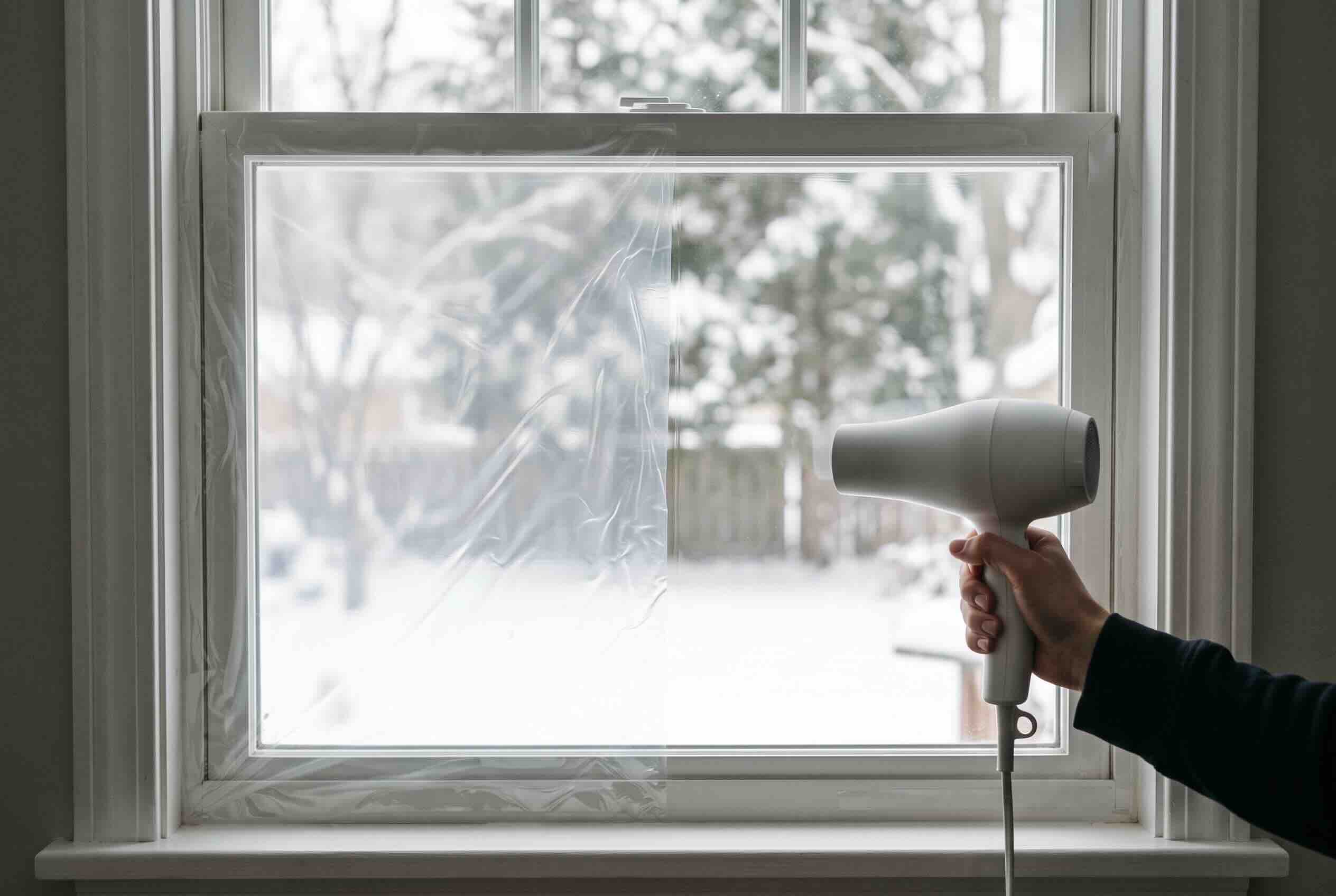 A hairdryer applying heat to shrink clear plastic insulating film tightly over a window pane.