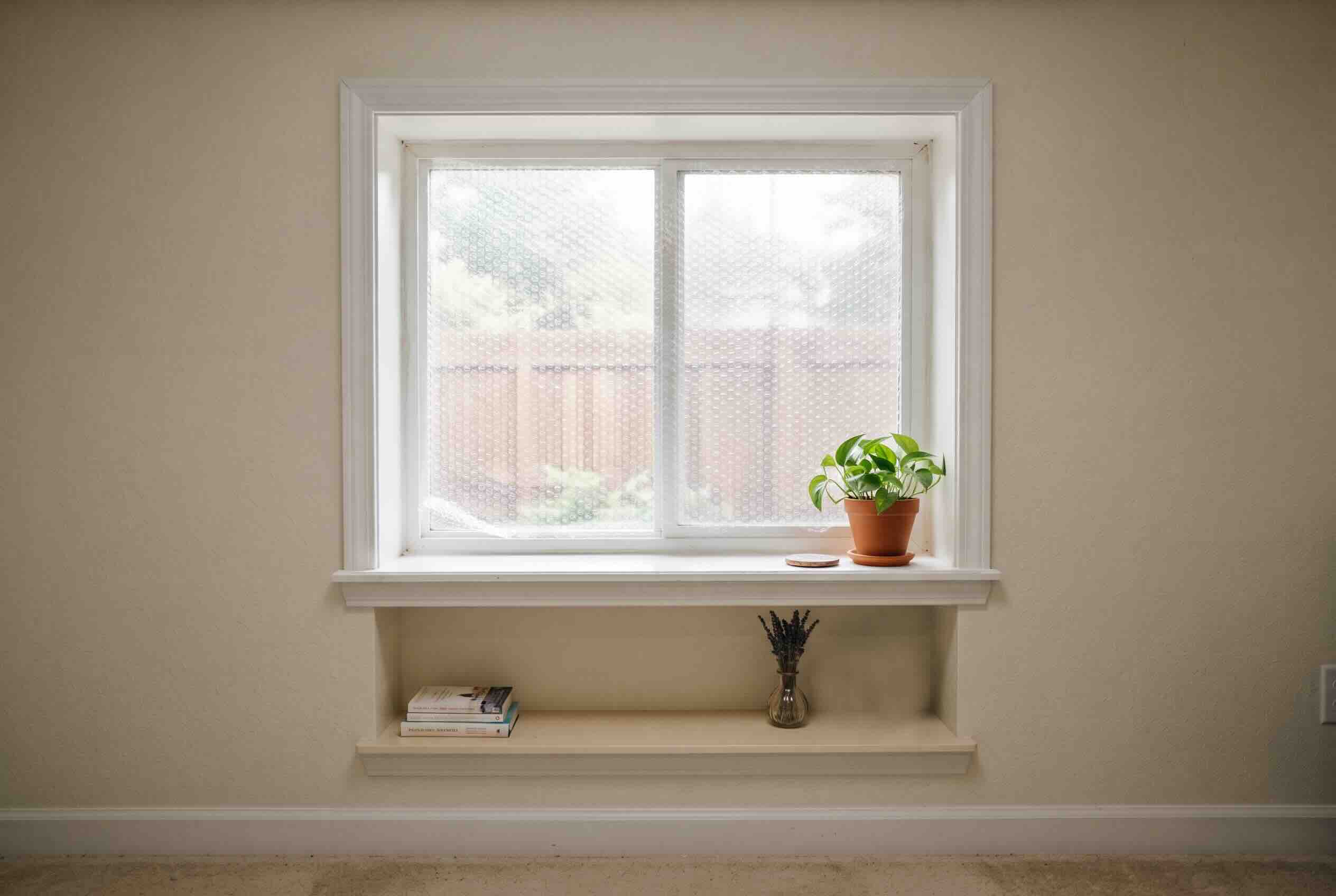 A layer of bubble wrap covering the glass of a window situated above a small shelf.