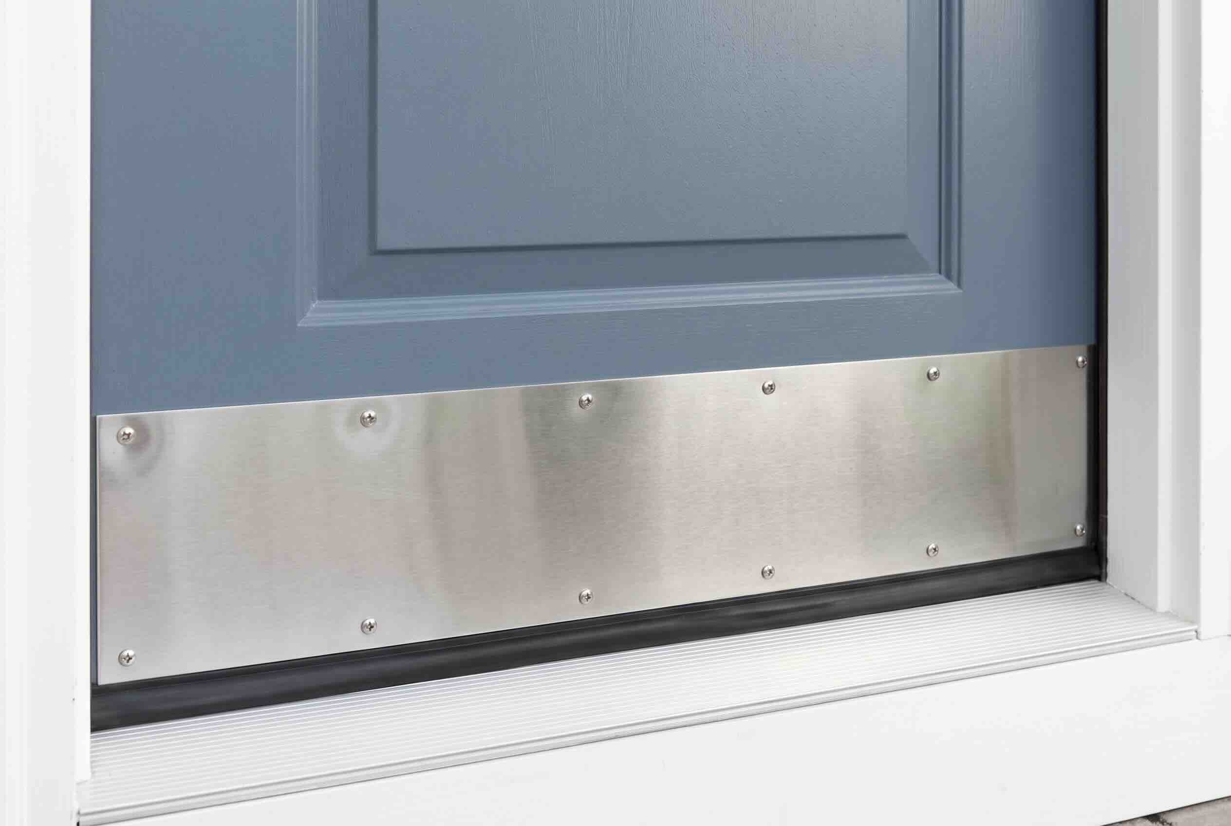 A rectangular sheet metal kick plate screwed into the bottom edge of a blue exterior door.