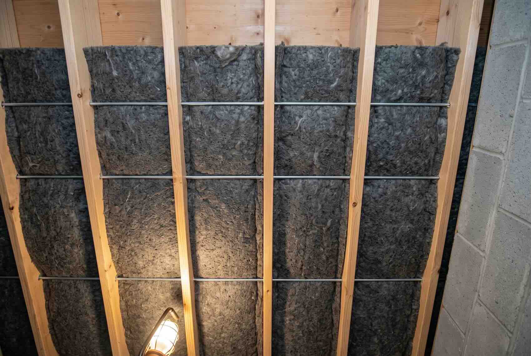 Dark grey mineral wool insulation batts installed tightly between wooden wall framing.